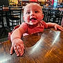 Laniey is registered to the contest to win money with this photo: baby, child, smiling, happy, table, wood, restaurant, high_chair, indoor, decorations, colorful, lights, celebration, face, person, clothing, arm, hand, mouth, tongue