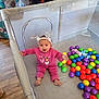 Laniey is registered to the contest to win money with this photo: baby, child, playpen, pink_clothing, reindeer_antlers, colorful_balls, indoor, flooring, wood_floor, toy, person, smiling, cute, infant, play_area, happy, headband, legs, sitting, expression
