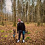 autumn, blue_harness, canine, casual_clothing, dog, forest, glasses, helmet, hiking, leash, leaves, man, moss, nature, outdoor, pet, smiling, standing, trees, walking