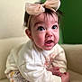 baby, child, headband, bow, pink_bow, sitting, clothing, white_sweater, floral_pants, chair, cream_chair, indoor, portrait, expression, cute, face, wide_eyes, person, soft_lighting, background_blur