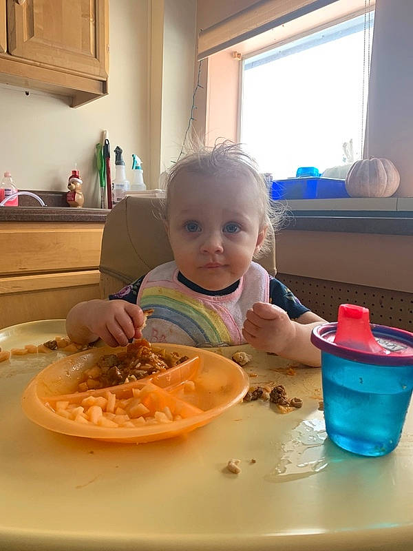 Veronica is registered to the contest to win money with this photo: baby, cabinetry, chair, child, comfort_food, cuisine, dish, drinkware, food, food_craving, ingredient, person, plate, recipe, sitting, smile, table, tableware, toddler, vegetable