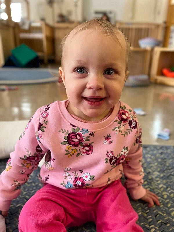 Veronica is registered to the contest to win money with this photo: baby, baby_toddler_clothing, cheek, child, chin, facial_expression, floor, flooring, fun, happy, iris, joy, magenta, pattern, person, pink, sitting, skin, sleeve, smile