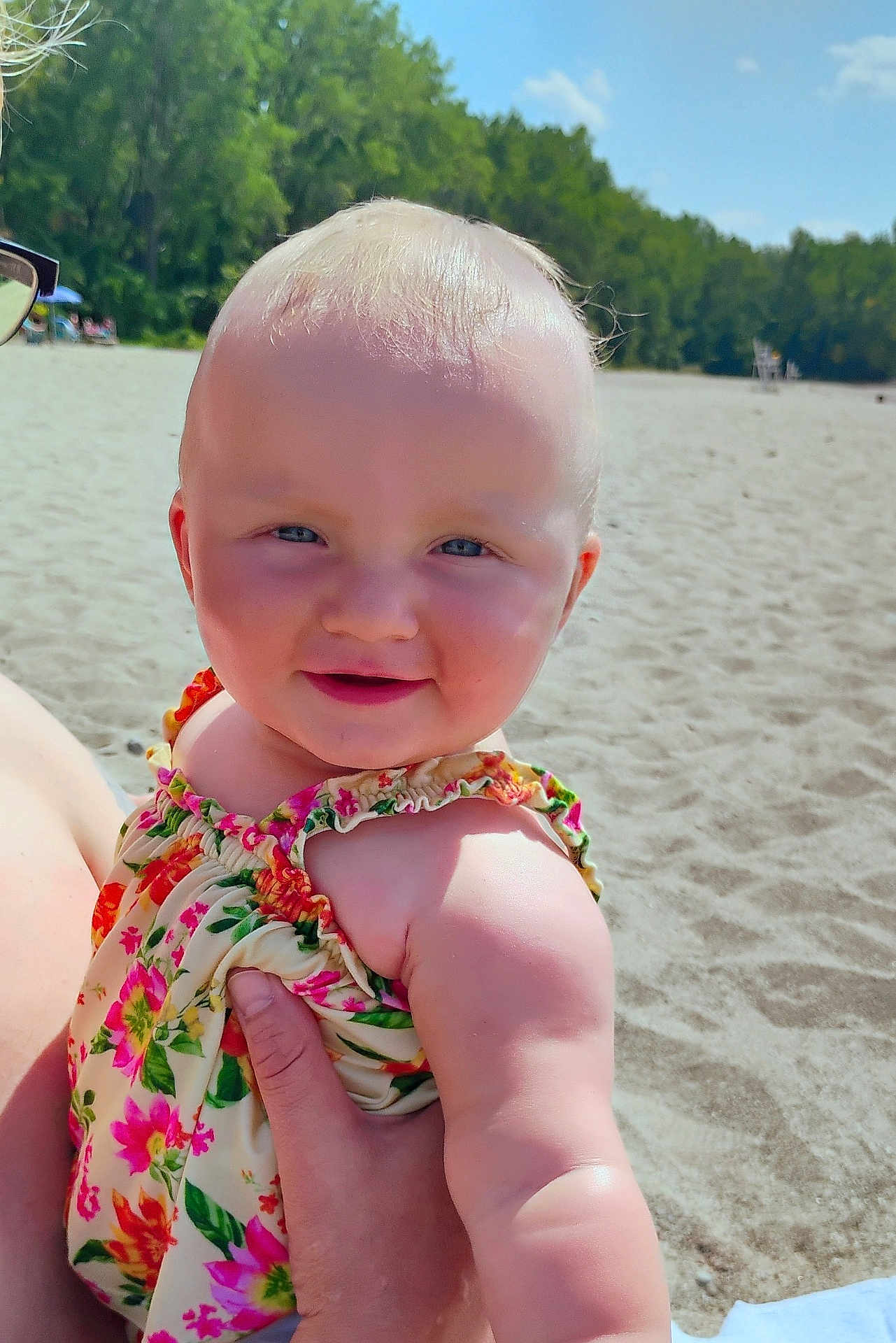 Aero is registered to the contest to win money with this photo: arm, baby, beach, blue_sky, child, cute, floral_dress, happy, head, holding, nature, outdoor, person, portrait, sand, skin, smiling, summer, sunny, trees