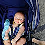 baby, blue_eyes, stroller, blanket, child, infant, seatbelt, outdoor, pavement, footwear, legs, summer_clothing, cute, person, baby_girl, sitting, soft_toy, candid, daylight, comfort