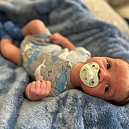 Andre joined the competition — help win amazing prizes! baby, infant, pacifier, blanket, blue, clothing, shark_pattern, onesie, hand, face, head, skin, newborn, lying_down, cozy, soft_texture, cute, indoor, portrait, child