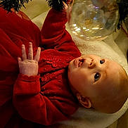 Bayley joined the competition — help win amazing prizes! baby, child, red_clothing, christmas_tree, ornament, holiday, curious, indoor, blanket, toddler, festive, smiling, face, hand, decorations, cozy, soft_lighting, seasonal, cute, portrait