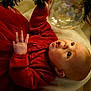 baby, child, red_clothing, christmas_tree, ornament, holiday, curious, indoor, blanket, toddler, festive, smiling, face, hand, decorations, cozy, soft_lighting, seasonal, cute, portrait