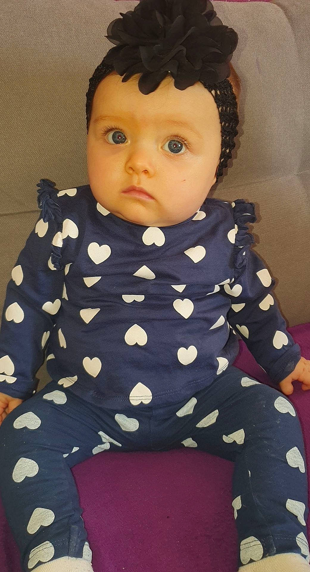 Zélie a rejoint le concours — aidez-le/la à gagner de superbes lots ! baby_toddler_clothing, black_hair, cheek, child, doll, eye, eyelash, face, fashion_design, head, knee, one_piece_garment, outerwear, pattern, pink, sitting, sleeve, thigh, toddler, toy