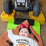 Raylynn joined the competition — help win amazing prizes! baby, infant, smiling, headband, red_bow, tools, screwdriver, wrench, toy_tractor, floor, clothing, long_sleeve, green_cushion, brown_cloth, indoor, child, happy, cute, playtime, football_theme