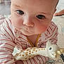 baby, infant, child, toy, giraffe_toy, striped_clothing, close_up, hand, floor_mat, indoor, curious, face, cute, playtime, person, young_child, soft_lighting, expression, head, crawling