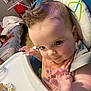 baby, high_chair, bib, mohawk, hand_gesture, face, eyes, indoor, toy, dog, bed, blanket, person, child, furniture, home, cute, expression, smile, clothing