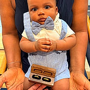 Jonas is registered to the contest to win money with this photo: baby, child, adult, hands, bow_tie, suspenders, clothing, wooden_box, rings, jewelry, portrait, indoor, person, seated, skin, nails, holding, cute, expression, closeup