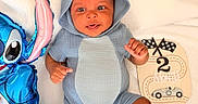 Jonas is registered to the contest to win money with this photo: baby, infant, blue_onesie, hooded_clothing, smiling, face, inflatable_toy, blue_toy, cartoon_character, wooden_sign, milestone_sign, 2_months, race_flags, race_car, blanket, soft_texture, cute, happy, portrait, child