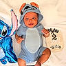 baby, infant, blue_onesie, hooded_clothing, smiling, face, inflatable_toy, blue_toy, cartoon_character, wooden_sign, milestone_sign, 2_months, race_flags, race_car, blanket, soft_texture, cute, happy, portrait, child