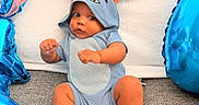 Jonas is registered to the contest to win money with this photo: baby, infant, blue_onesie, orange_ears, balloons, blue_balloons, fists_up, curious_expression, sitting, gray_surface, white_backdrop, cute, child, portrait, indoor, plush, soft_texture, happy, young_child, photography