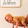 baby, infant, yawning, knitted_clothing, hand, arm, sign, text, wall, cozy, newborn, cute, portrait, human, skin, sleepy, welcoming, family, indoor, soft_light
