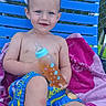 child, toddler, baby_bottle, blue_chair, pink_towel, swim_trunks, outdoor, poolside, wet_hair, smiling, summer, relaxing, fence, grass, water, person, sitting, happy, sunny, drink