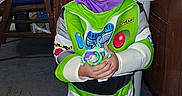 Bryson is registered to the contest to win money with this photo: child, costume, buzz_lightyear, toy, barefoot, smile, indoor, carpet, wood_paneling, furniture, chair, boxes, curtains, blue_eyes, purple_hood, green, white, playful, person, portrait