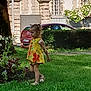 child, girl, yellow_dress, flower, grass, outdoor, park, tree, car, building, hedge, sandals, summer, walking, greenery, daylight, nature, cute, side_view, playful
