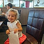 Elyne participe au concours pour gagner de l'argent avec cette photo : child, girl, smiling, curly_hair, white_top, coral_skirt, chair, restaurant, woman, dining, napkin, happy, indoor, plant, window, table, brown_leather, seat, casual, portrait