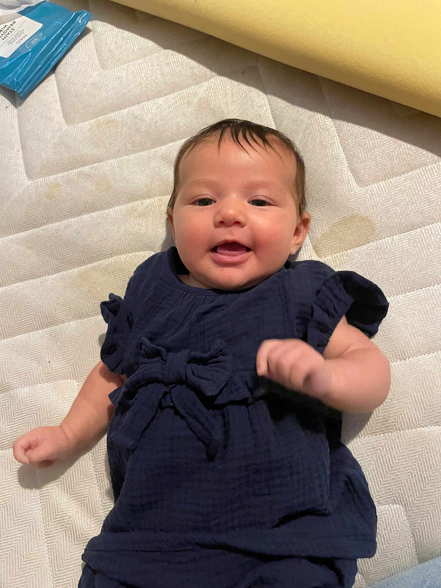 Mila joined the competition — help win amazing prizes! baby, infant, smiling, lying_down, blue_clothing, mattress, textured_surface, cute, child, playful, young, face, small_hands, happy, indoors, fabric, soft_lighting, person, toddler, casual