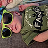 baby, newborn, infant, child, sunglasses, green_sunglasses, portrait, lying_down, couch, blanket, clothing, green_shirt, printed_shirt, face, eyes, nose, mouth, hand, indoor, funny