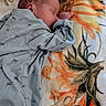 newborn, baby, sleeping, infant, portrait, face, closed_eyes, peaceful, onesie, blue_clothing, airplane_pattern, blanket, floral_blanket, bed, indoors, resting, curled_up, fist, cozy, photography