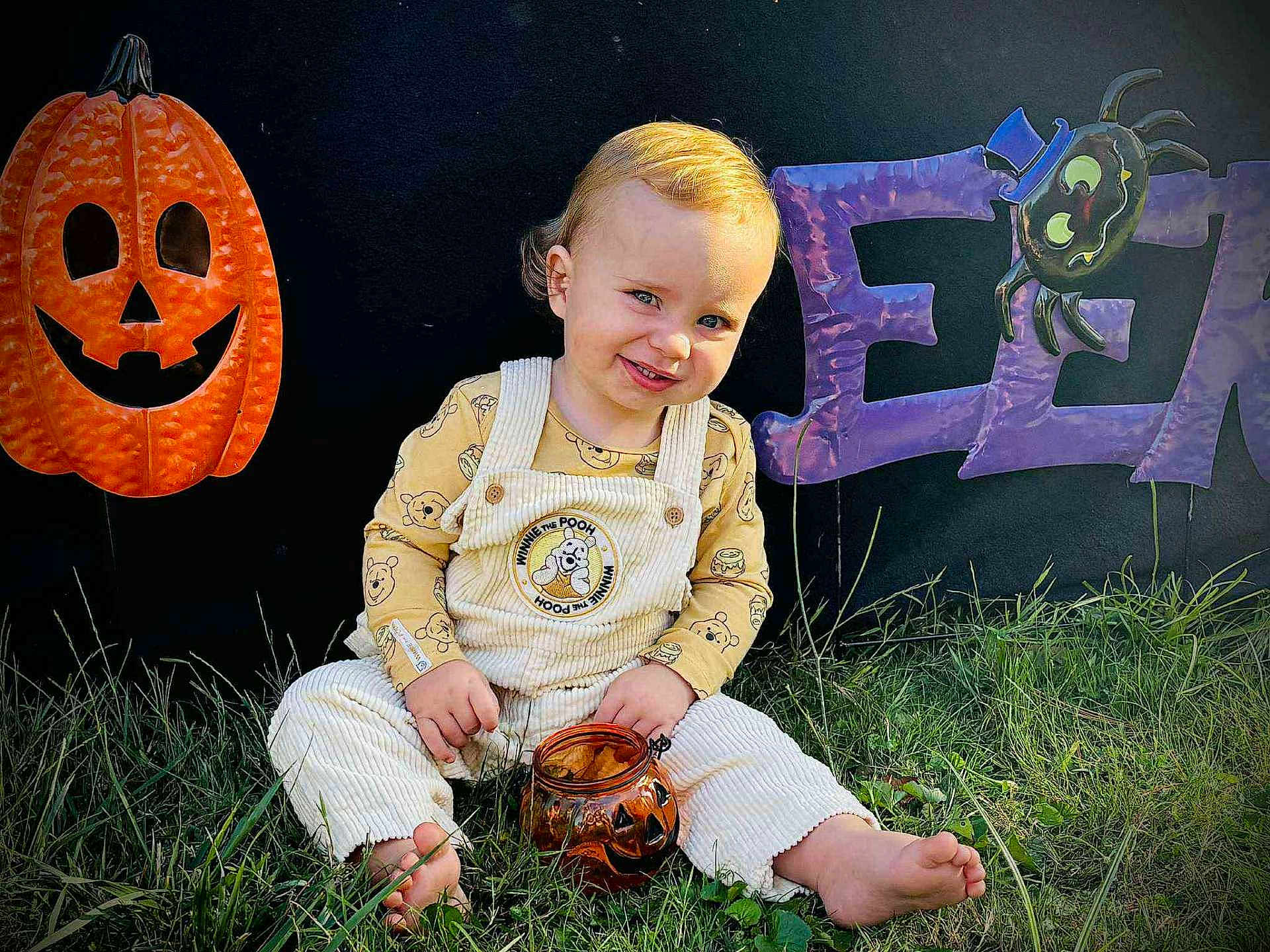 Phoniex is registered to the contest to win money with this photo: child, toddler, grass, barefoot, winnie_the_pooh, overalls, pumpkin, jack_o_lantern, halloween, decorations, smiling, outdoor, cute, jar, toy, orange, purple, spider, festive, holiday
