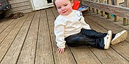Hazel Hamby is registered to the contest to win money with this photo: child, porch, wooden_deck, sweatshirt, pants, white_shoes, door, pet_flap, outdoor, curious_expression, small_pony_tail, casual_clothing, wooden_railing, vehicle, toy, floor, hand, sitting, daylight, person