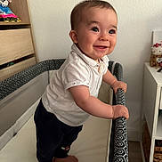 Manoa a rejoint le concours — aidez-le/la à gagner de superbes lots ! baby, child, playpen, standing, drool, smile, happy, indoor, clothing, white_shirt, pants, barefoot, nursery, furniture, toy, face, person, room, expression, curious