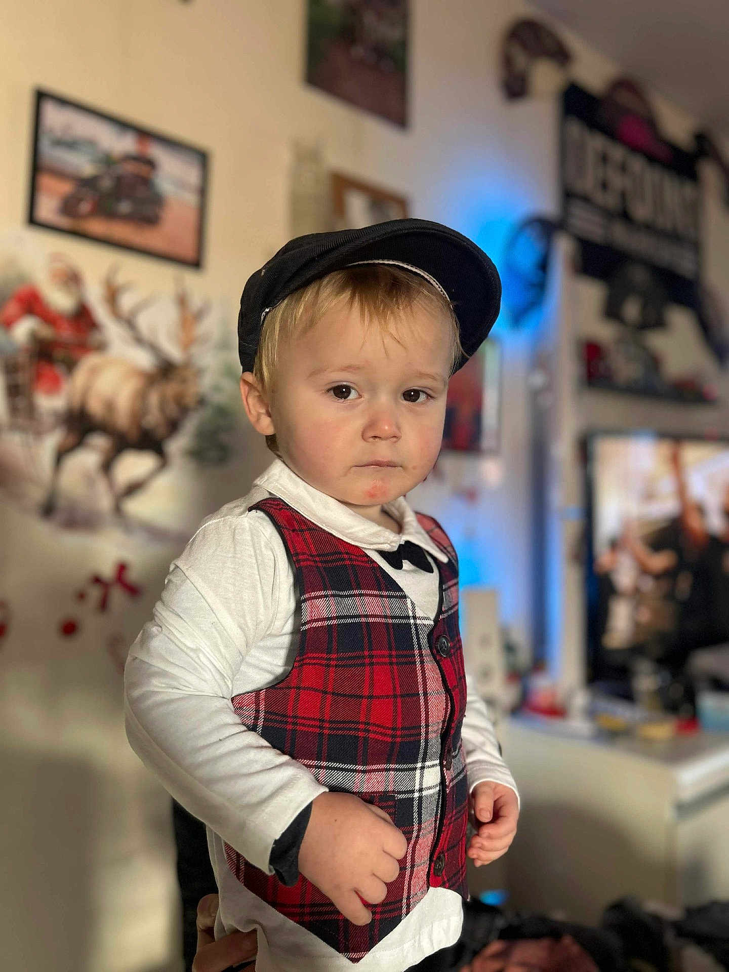 Cylian a rejoint le concours — aidez-le/la à gagner de superbes lots ! child, toddler, boy, cap, flat_cap, plaid_vest, bow_tie, portrait, indoor, living_room, holiday_decor, moose_painting, framed_picture, tv_screen, hands, expression, cute, shallow_depth_of_field, blurred_background, casual_clothing