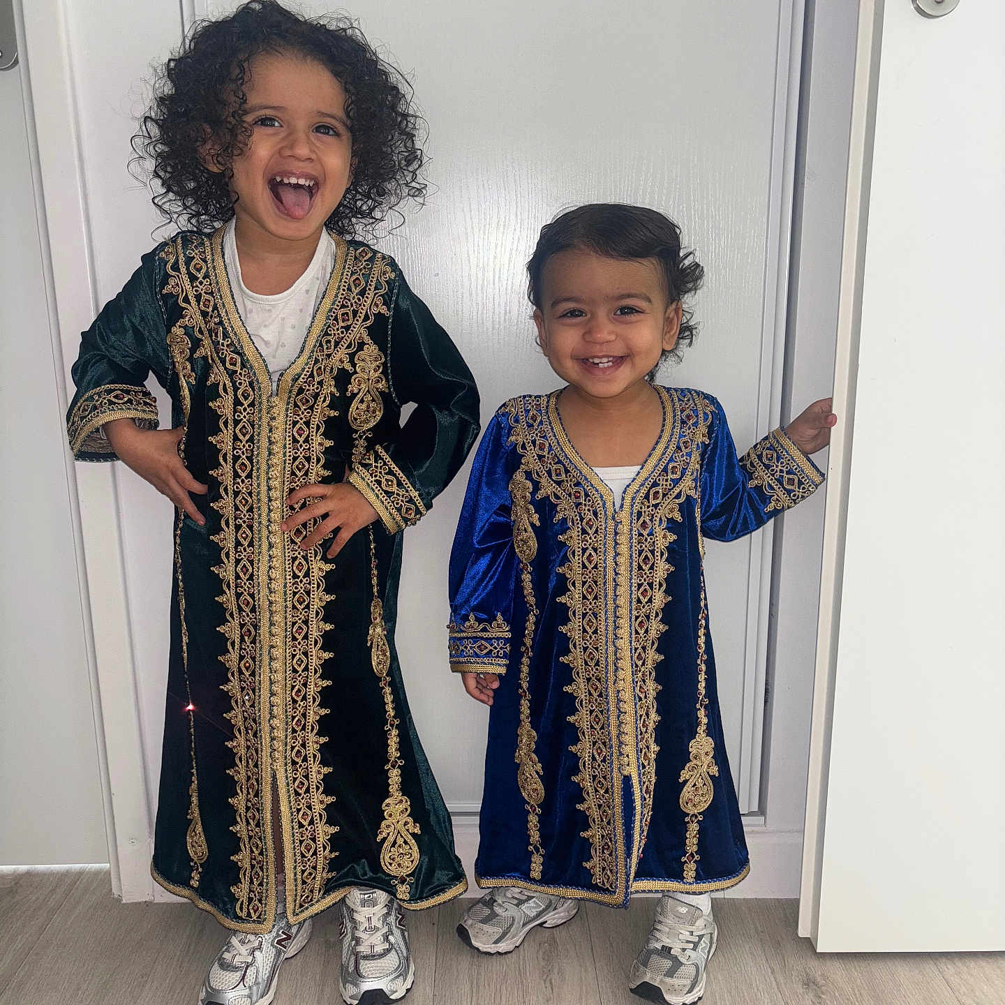 Layah a rejoint le concours — aidez-le/la à gagner de superbes lots ! child, children, smiling, traditional_clothing, dress, curly_hair, standing, door, floor, white_background, happy, sneakers, indoors, portrait, cute, two_people, young, playful, full_body, person