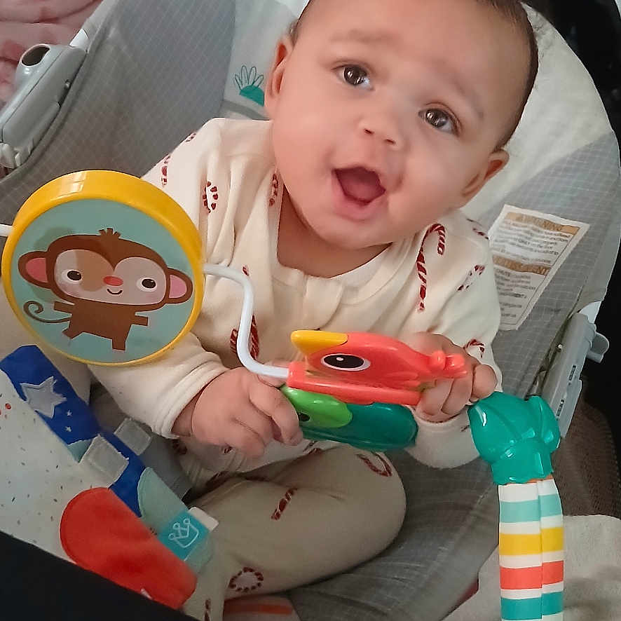 Carmine is registered to the contest to win money with this photo: baby, blanket, child, clothing, colorful, cute, expression, face, happy, heart_pattern, indoor, infant, person, play, playpen, portrait, sitting, smiling, toy, young