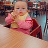 Carmine is registered to the contest to win money with this photo: baby, butterfly_stickers, casual, child, clapping, curious, dining, face, floor, furniture, hands, high_chair, indoor, people, pink_clothing, restaurant, seated, table, wooden_chair, yellow_bib