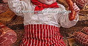 éliot a rejoint le concours — aidez-le/la à gagner de superbes lots ! baby, chef_hat, red_scarf, striped_apron, sausage, cured_meat, charcuterie, wooden_board, cutting_board, rustic, food, smile, costume, infant, clothing, person, portrait, kitchen, gourmet, meat