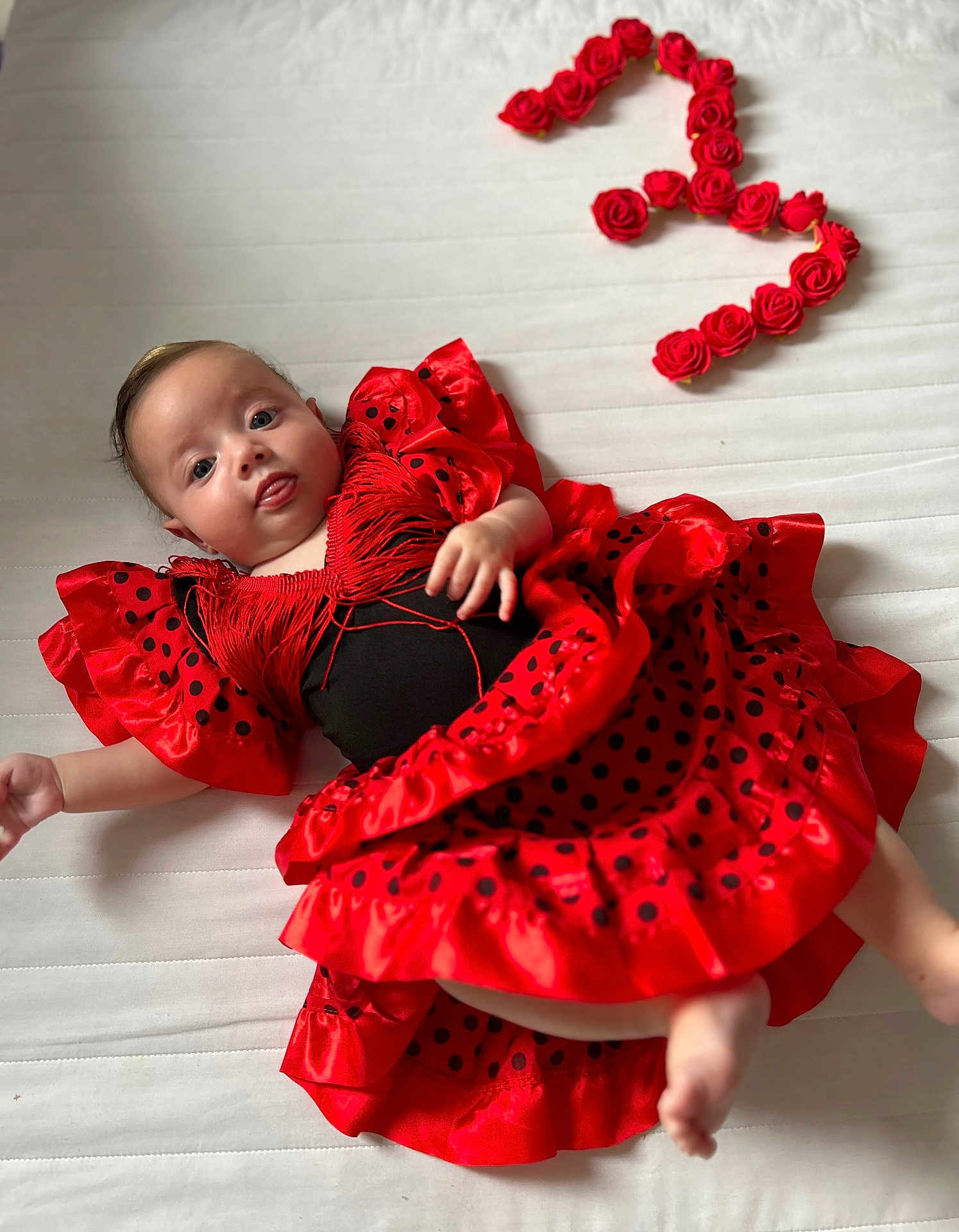 Rosalia a rejoint le concours — aidez-le/la à gagner de superbes lots ! baby, celebration, child, clothing, colorful, cute, dress, fabric, flamenco_style, happy, infant, lying_down, number_three, person, polka_dot, portrait, red_dress, roses, tongue_out, white_background