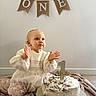 Lysia a rejoint le concours — aidez-le/la à gagner de superbes lots ! baby, child, cake, birthday, first_birthday, white_dress, lace, clapping, blue_eyes, blanket, banner, decoration, homemade_cake, celebration, indoor, floor, person, cute, happy, party