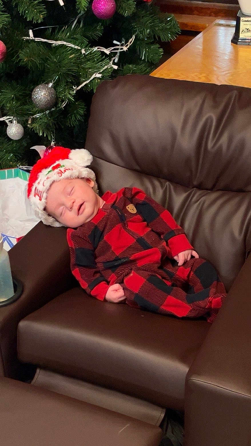 Grayson is registered to the contest to win money with this photo: baby, sleeping, plaid_pajamas, santa_hat, christmas_tree, ornaments, brown_leather_chair, holiday, festive, cozy, infant, indoor, holiday_decor, peaceful, child, cute, relaxing, seasonal, celebration, home