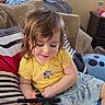 child, baby, toddler, couch, indoor, yellow_shirt, floral_skirt, striped_pillow, curtains, window, device, playing, happy, smiling, furniture, home, water_bottle, blanket, cute, portrait