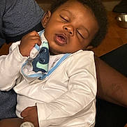Kyson joined the competition — help win amazing prizes! baby, sleeping, infant, clothing, hand, adult, bottle, indoor, wooden_floor, pacifier, closeup, person, peaceful, face, curly_hair, white_onesie, comfort, rest, nap, holding
