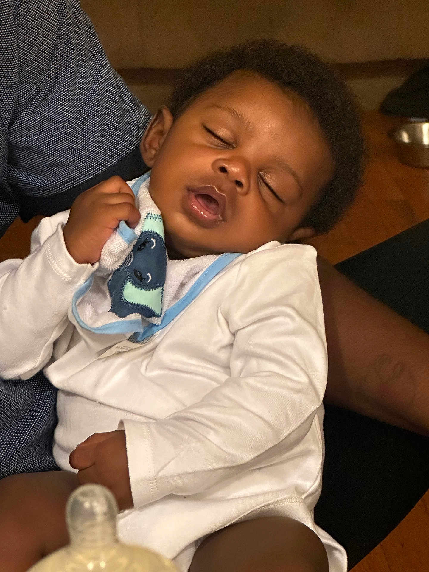 Kyson joined the competition — help win amazing prizes! baby, sleeping, infant, clothing, hand, adult, bottle, indoor, wooden_floor, pacifier, closeup, person, peaceful, face, curly_hair, white_onesie, comfort, rest, nap, holding