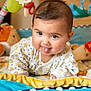 baby, infant, tongue_out, playmat, plush_toys, colorful, cute, child, smiling, indoors, soft_toys, person, face, clothing, happy, playful, young_child, baby_girl, baby_boy, closeup