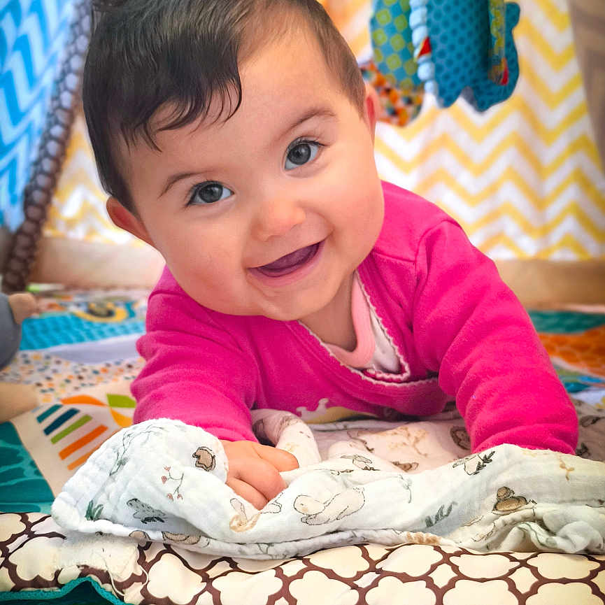 Charline a rejoint le concours — aidez-le/la à gagner de superbes lots ! baby, blanket, bright, cheerful, child, colorful, cute, face, happy, indoor, infant, patterned, pink_clothing, play_mat, playtime, portrait, smile, soft_toys, toddler, toy