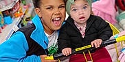 Keziah joined the competition — help win amazing prizes! child, baby, shopping_cart, store, aisle, clothing, headband, curly_hair, smile, happy, retail, indoor, yellow_cart, jacket, pants, socks, person, toddler, sibling, family