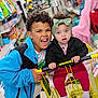 child, baby, shopping_cart, store, aisle, clothing, headband, curly_hair, smile, happy, retail, indoor, yellow_cart, jacket, pants, socks, person, toddler, sibling, family