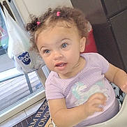 Keziah joined the competition — help win amazing prizes! toddler, child, high_chair, purple_shirt, unicorn, curly_hair, pink_hair_ties, kitchen, microwave, plastic_bag, door, floor_tile, mat, window, cabinet, table, indoor, person, baby, home