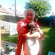 Azia participe au concours pour gagner de l'argent avec cette photo : man, puppy, dog, outdoor, backyard, grass, tree, sunlight, orange_jacket, pet, holding, watering_can, garden, fence, house, shadow, clothing, portrait, daylight, casual