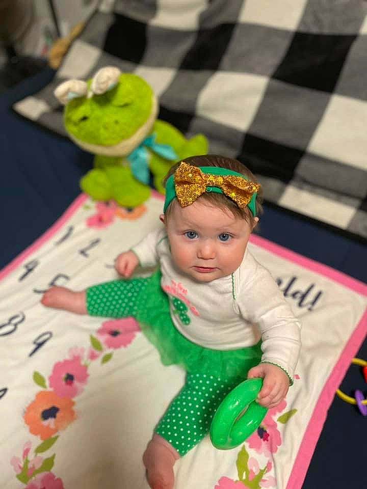 Riley is registered to the contest to win money with this photo: animation, baby, baby_products, baby_toddler_clothing, baby_toys, child, costume, doll, event, fashion_accessory, fictional_character, fun, happy, headwear, linens, party_supply, pattern, person, play, sitting