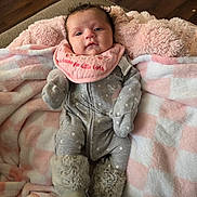 Brynlee is registered to the contest to win money with this photo: baby, infant, blanket, pink, grey_onesie, boots, fur_trim, polka_dots, face, floor, wooden_floor, plush_toy, furniture, indoor, cute, child, soft_texture, clothing, portrait, lying_down