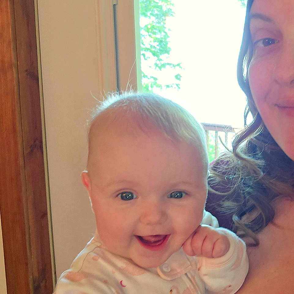 Liliana joined the competition — help win amazing prizes! baby, child, clothing, cute, face, happy, holding, home, indoor, infant, joyful, light, natural_light, onesie, person, portrait, smiling, swan_pattern, window, woman